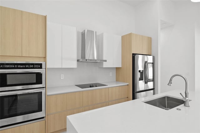 kitchen with white cabinets, wall chimney range hood, sink, light brown cabinetry, and stainless steel appliances