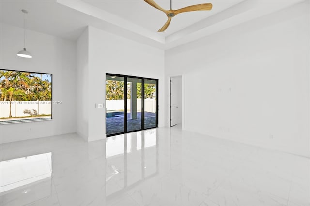 empty room featuring a tray ceiling, ceiling fan, a towering ceiling, and a healthy amount of sunlight