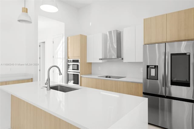 kitchen featuring white cabinetry, wall chimney range hood, decorative light fixtures, a center island with sink, and appliances with stainless steel finishes