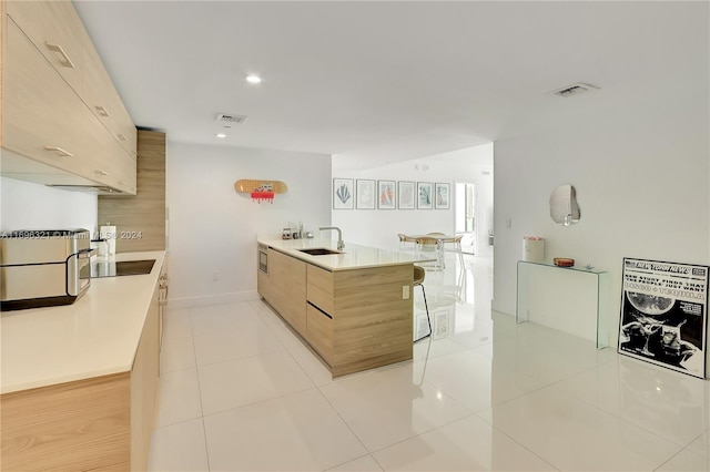 kitchen featuring light brown cabinets, sink, a kitchen bar, black electric cooktop, and light tile patterned floors