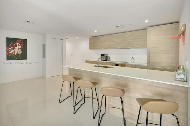 kitchen featuring a breakfast bar, light brown cabinets, electric panel, sink, and light tile patterned floors