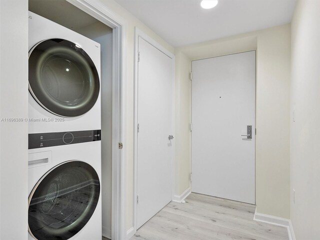 laundry room featuring stacked washing maching and dryer and light hardwood / wood-style flooring