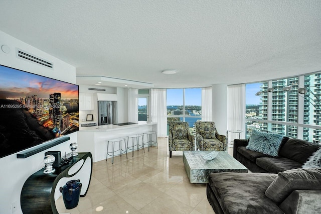 tiled living room featuring a textured ceiling, a water view, and floor to ceiling windows