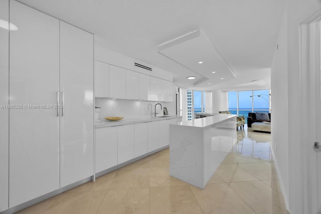 kitchen featuring sink, light tile patterned floors, a kitchen island, white cabinets, and a water view