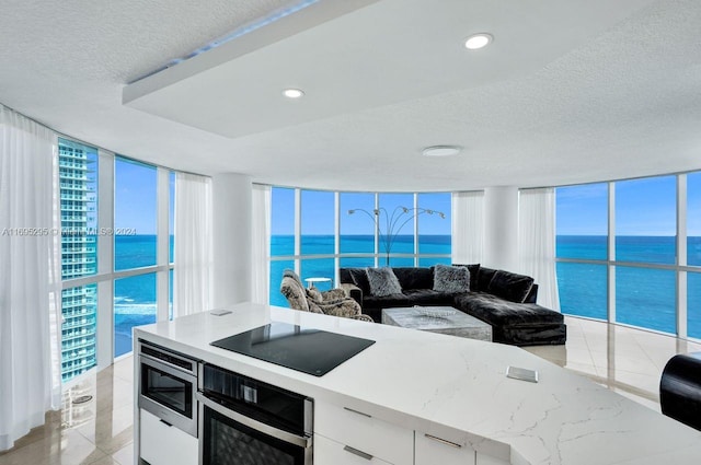 kitchen with white cabinets, a water view, a healthy amount of sunlight, a wall of windows, and stainless steel appliances