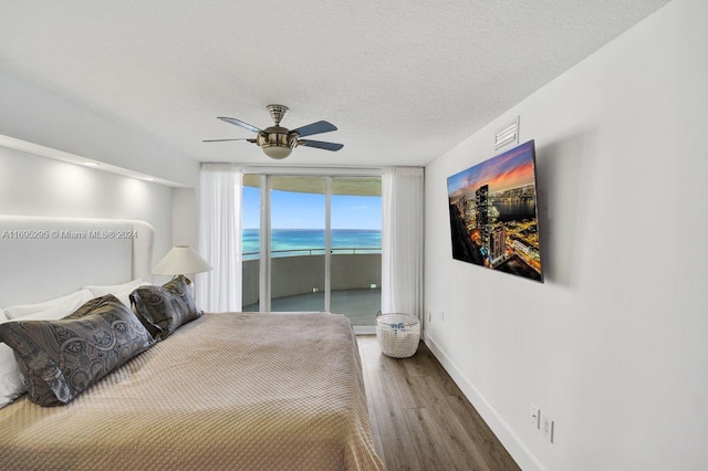 bedroom featuring access to outside, hardwood / wood-style flooring, ceiling fan, a textured ceiling, and a wall of windows