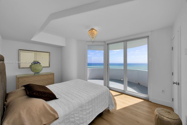 bedroom featuring access to exterior, light hardwood / wood-style floors, a water view, and a view of the beach