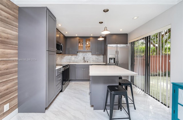 kitchen with sink, pendant lighting, decorative backsplash, a kitchen island, and appliances with stainless steel finishes