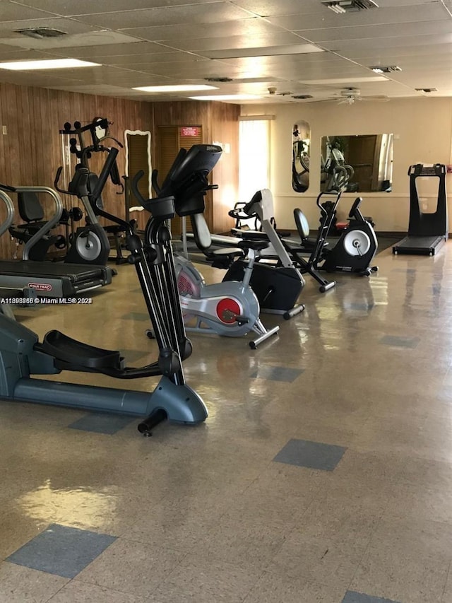 gym featuring a paneled ceiling and wooden walls