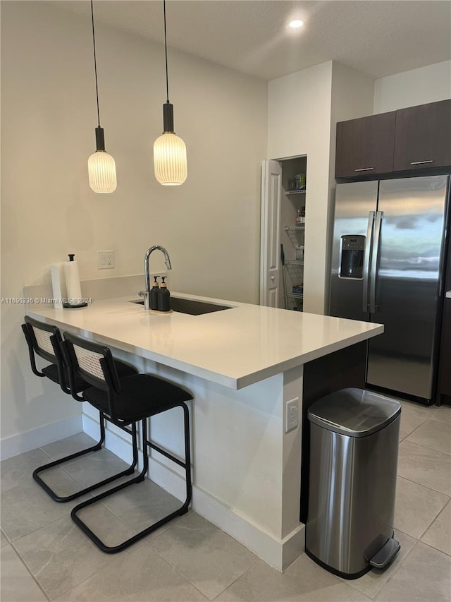 kitchen featuring dark brown cabinetry, sink, pendant lighting, stainless steel fridge with ice dispenser, and a breakfast bar area