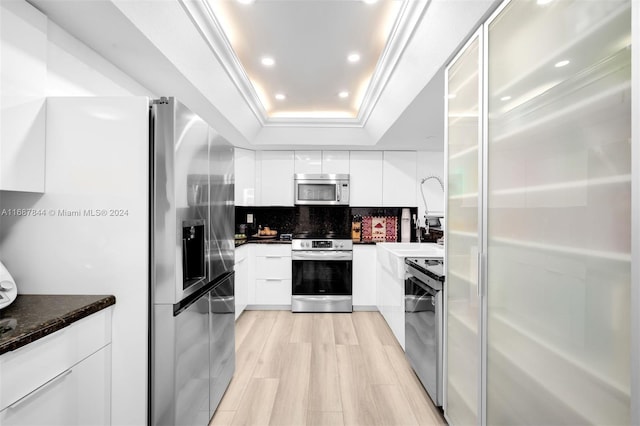 kitchen featuring tasteful backsplash, light hardwood / wood-style floors, a tray ceiling, white cabinets, and appliances with stainless steel finishes