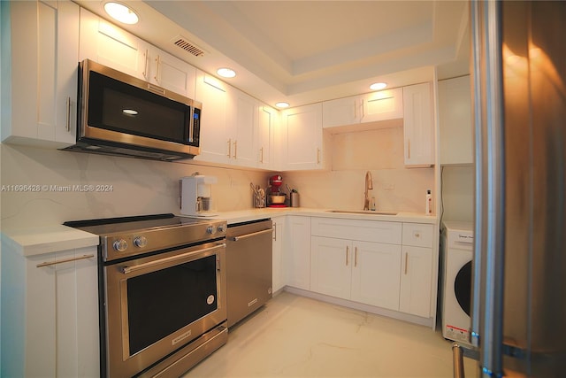 kitchen with washer / dryer, sink, white cabinets, and appliances with stainless steel finishes