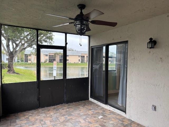 unfurnished sunroom with ceiling fan and a water view