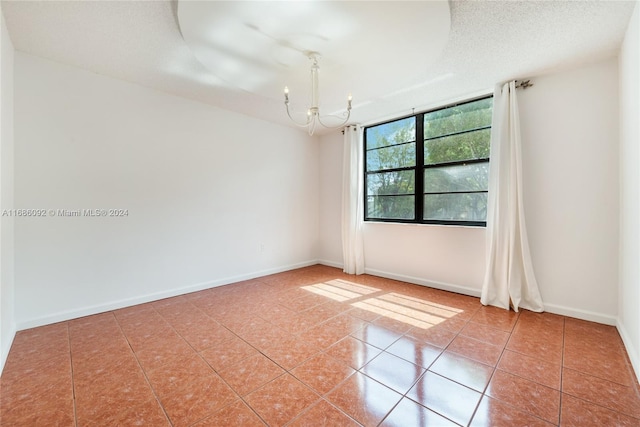 tiled empty room featuring a textured ceiling and a notable chandelier