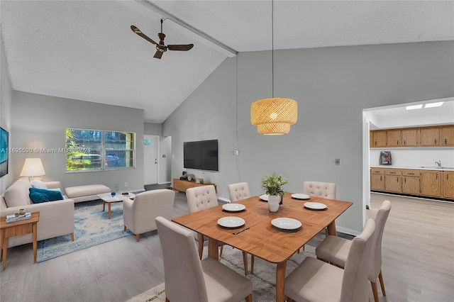 dining room featuring ceiling fan, sink, high vaulted ceiling, light hardwood / wood-style floors, and a textured ceiling