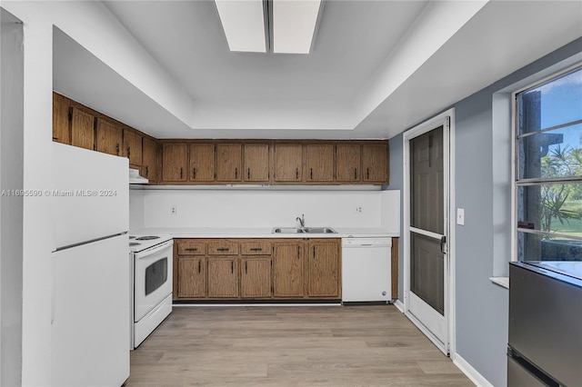 kitchen with light hardwood / wood-style floors, a raised ceiling, white appliances, and sink