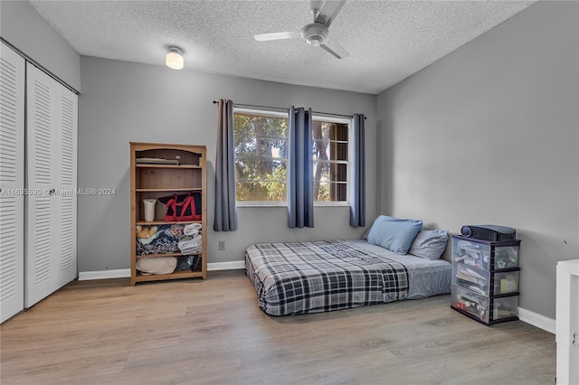 bedroom with ceiling fan, light hardwood / wood-style floors, a textured ceiling, and a closet