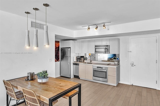 kitchen with pendant lighting, white cabinets, sink, light hardwood / wood-style flooring, and appliances with stainless steel finishes