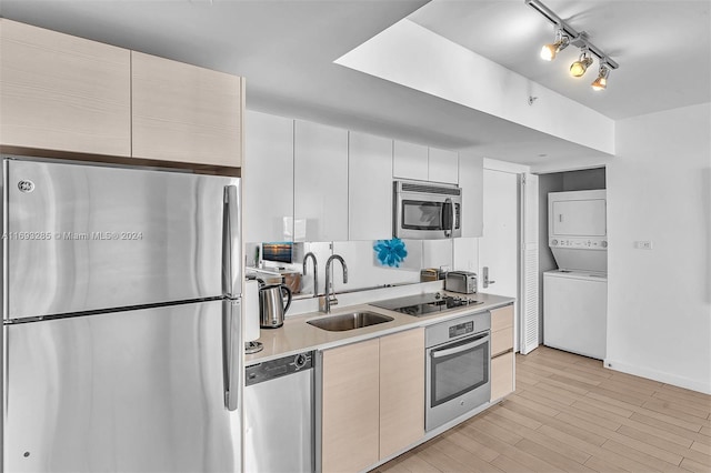 kitchen with sink, light hardwood / wood-style floors, white cabinets, stacked washer and clothes dryer, and appliances with stainless steel finishes