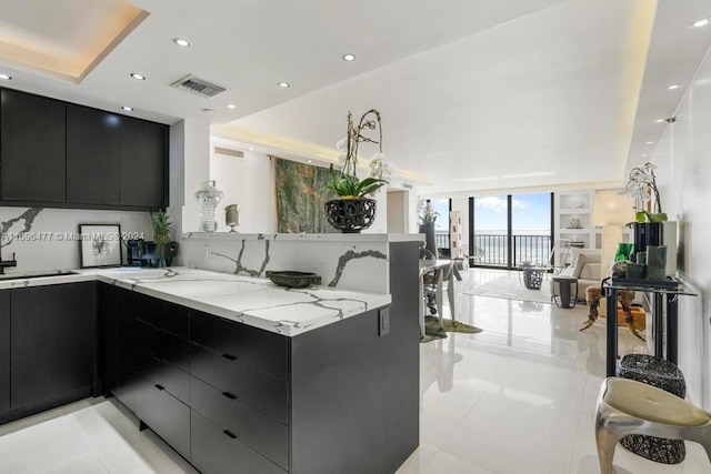 kitchen featuring kitchen peninsula, light stone countertops, expansive windows, and light tile patterned flooring