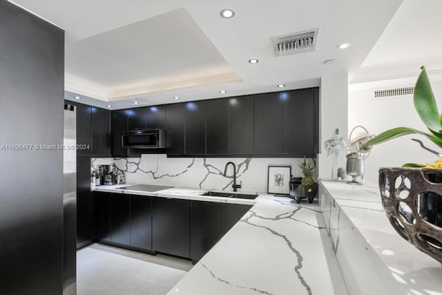 kitchen featuring black appliances, sink, tasteful backsplash, a tray ceiling, and light stone counters