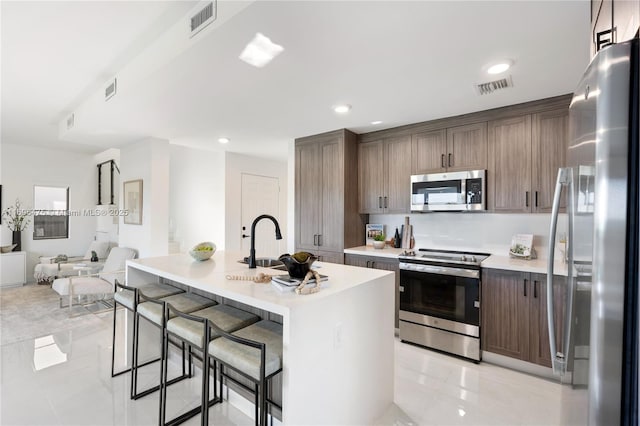 kitchen with visible vents, a kitchen bar, open floor plan, appliances with stainless steel finishes, and light countertops