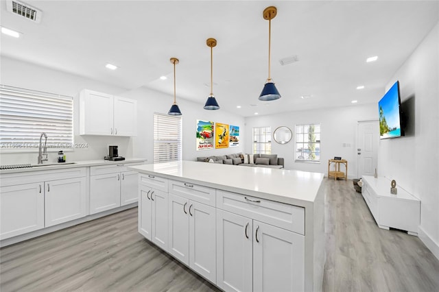 kitchen featuring pendant lighting, sink, light hardwood / wood-style flooring, a kitchen island, and white cabinetry