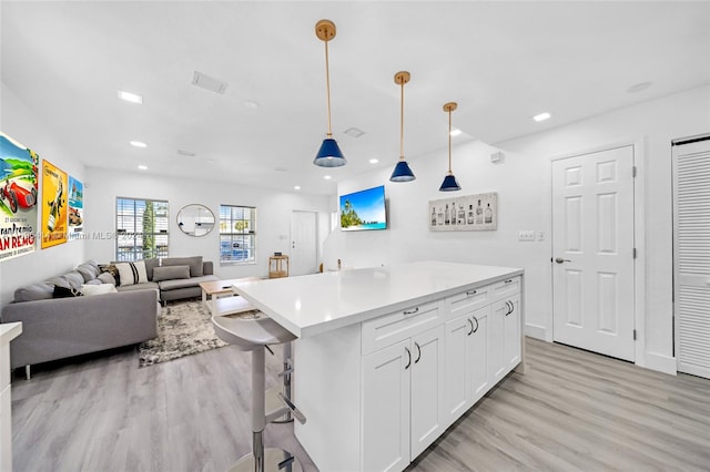 kitchen featuring white cabinets, decorative light fixtures, a kitchen island, and light hardwood / wood-style floors