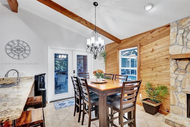 tiled dining space featuring french doors, sink, beam ceiling, wooden walls, and a fireplace