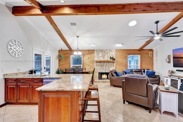 kitchen featuring a breakfast bar area, vaulted ceiling with beams, wooden walls, light stone counters, and decorative light fixtures