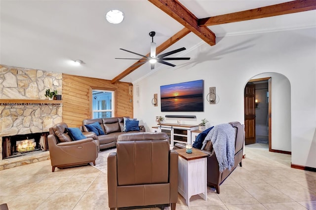 living room with a fireplace, wood walls, lofted ceiling with beams, light tile patterned floors, and ceiling fan