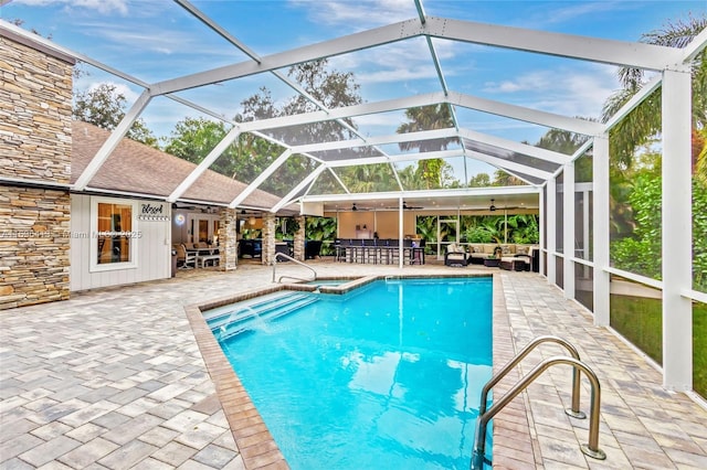 view of swimming pool with glass enclosure, a patio area, ceiling fan, and a bar