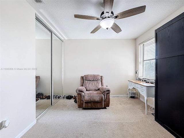 living area with ceiling fan, light carpet, and a textured ceiling