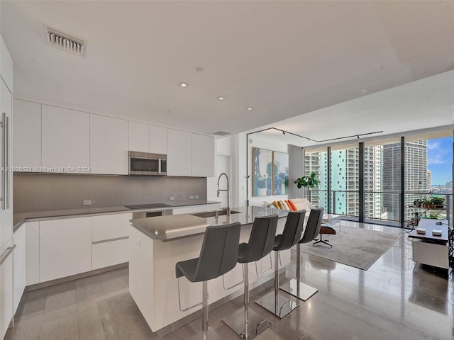 kitchen with a center island with sink, expansive windows, white cabinets, and a wealth of natural light