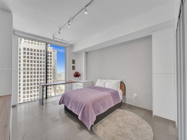 bedroom featuring concrete floors, track lighting, and floor to ceiling windows