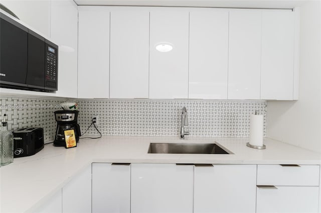 kitchen with tasteful backsplash, light stone countertops, sink, and white cabinets