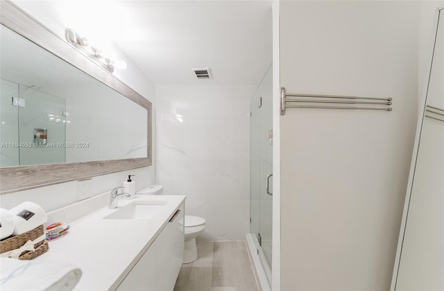 bathroom featuring a shower with door, vanity, and toilet