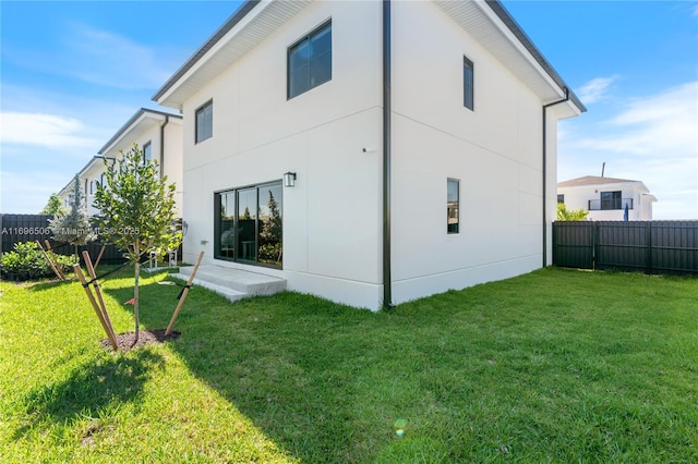 rear view of house with a yard, fence, and stucco siding