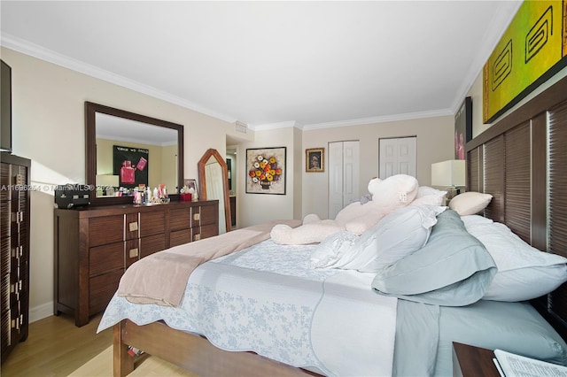 bedroom featuring crown molding, light hardwood / wood-style flooring, and multiple closets