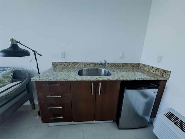 kitchen featuring light stone countertops, stainless steel fridge, dark brown cabinetry, sink, and light tile patterned flooring