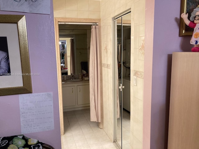 corridor featuring light tile patterned floors, tile walls, and sink