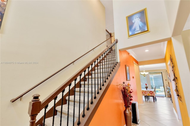 staircase featuring tile patterned flooring, ornamental molding, and an inviting chandelier