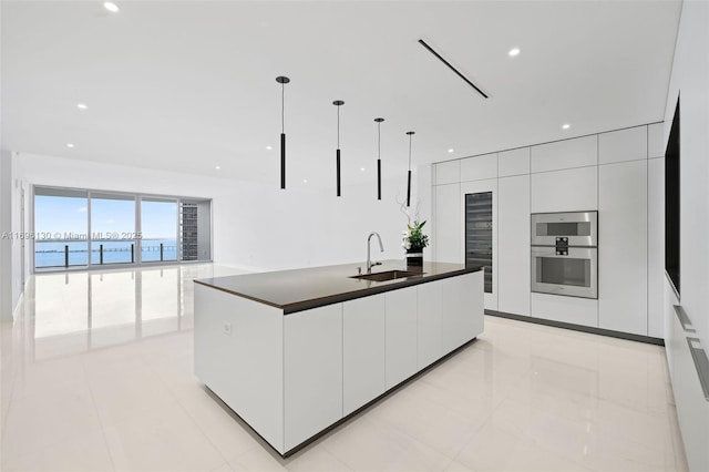 kitchen featuring modern cabinets, a sink, pendant lighting, dark countertops, and white cabinets