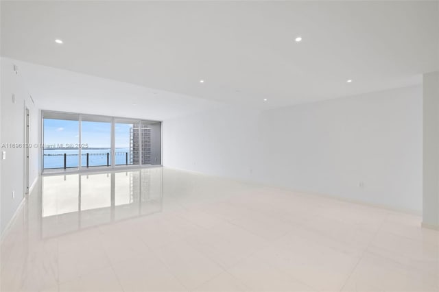 unfurnished room with floor to ceiling windows, recessed lighting, and a water view
