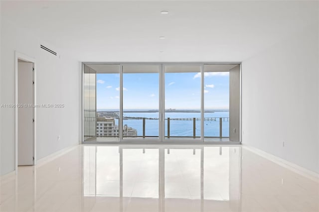 tiled empty room with a water view, floor to ceiling windows, and baseboards