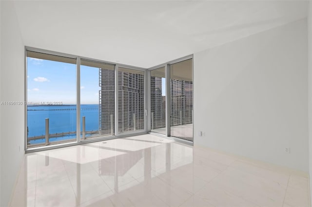 tiled empty room featuring a water view and expansive windows