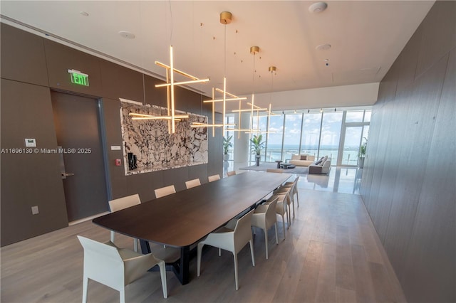 dining space featuring a wall of windows, light wood-style floors, and wood walls