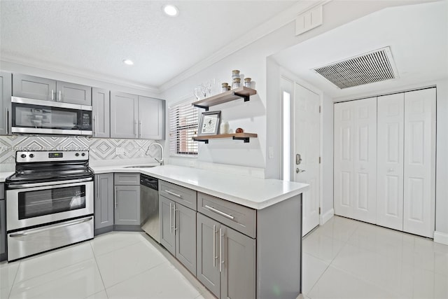 kitchen with gray cabinetry, sink, stainless steel appliances, a textured ceiling, and decorative backsplash