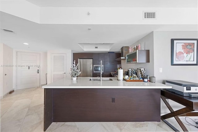 kitchen with appliances with stainless steel finishes, a kitchen breakfast bar, wall chimney exhaust hood, dark brown cabinetry, and sink