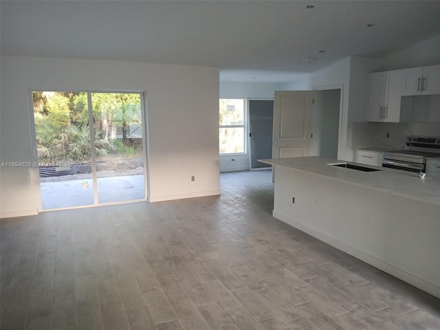 kitchen featuring baseboards, stainless steel electric range, light countertops, light wood-style floors, and white cabinetry